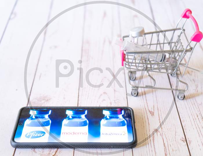 Mobile Phone Showing Vaccines Choices Covishield Covaxin Astrazeneca Moderna Pfizer With Small Shopping Cart With Syringe And Vial Showing Online Purchase And Home Innoculation For Covid 19 Coronavirus Pandemic