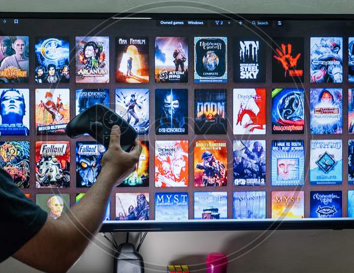 Man Holding A Steam Controller In Front Of The Steam Good Old Games Gog Epic Store Library Screen Choosing A Game To Play For Entertainment Leisure Addiction