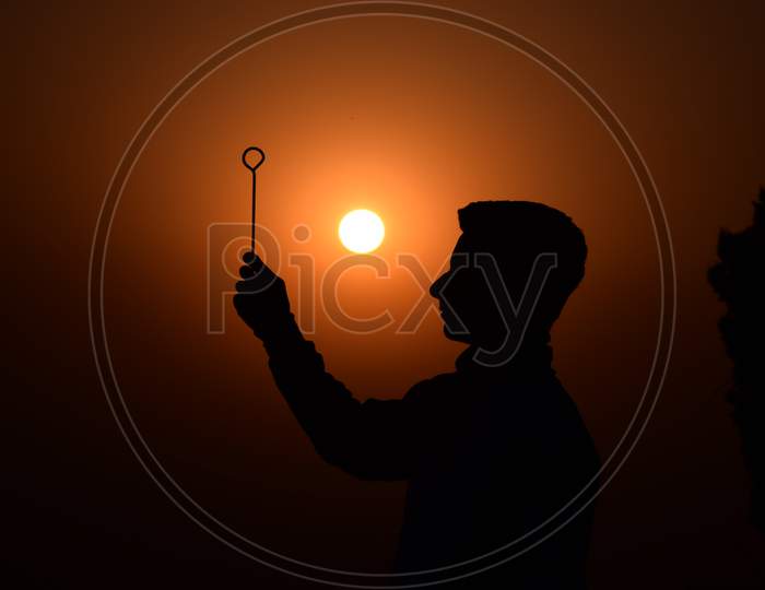 Boy Holds A Stick In His Hand. Beautiful Orange Sunset In Summer. Selective Focus, Selective Focus On Subject, Background Blur