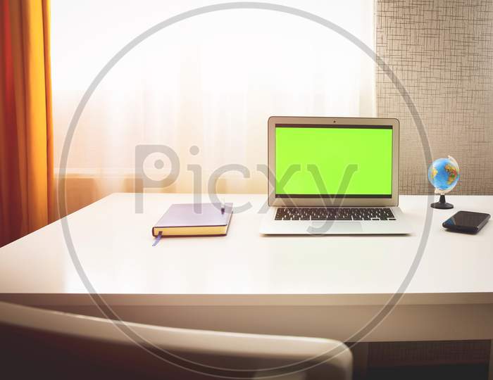 Green Screen Laptop Computer Sitting On A Home Work Desk Next To Notebook, Spring Flowers And World Globe Stand. Concept Minimalist Digital Student Work Space