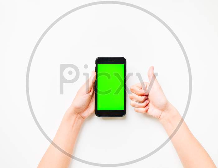 Woman Hand Shows Mobile Smartphone With Green Screen In Vertical Position Isolated On Green Background With Thumbs Up Finger. Mock Up Mobile Screen Blank Space