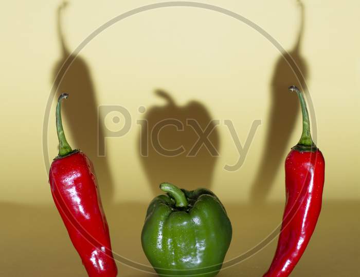 Dramatic Evil Picture Of Chilli And Capsicum ( Peppers ) With Shadow Falling On Background. Creative Vegetable Photography. Vegetable Shown In A Evil Way.