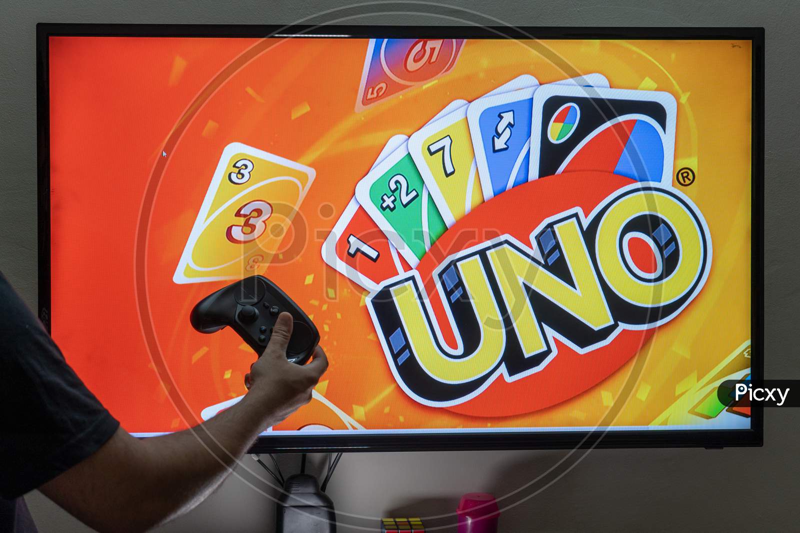 Man Holding Controller In Front Of A Screen Playing The Popular Card Game Uno Which Has Been Converted To An Online Application For Players To Enjoy