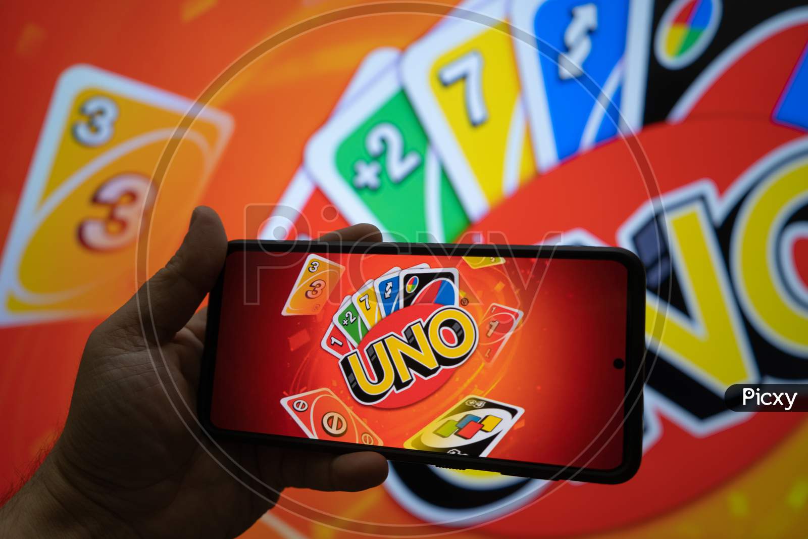 Man Holding A Mobile Phone With An Application Allowing Them To Play The Popular Card Game Uno During Travel Online With Players Worldwide