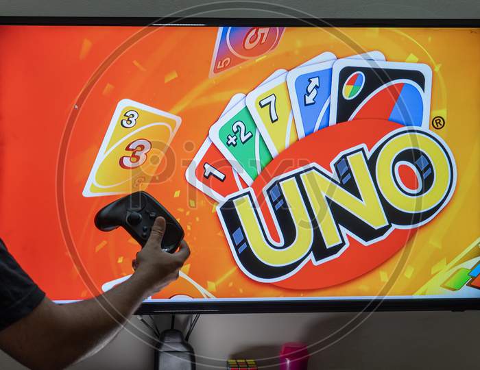 Man Holding Controller In Front Of A Screen Playing The Popular Card Game Uno Which Has Been Converted To An Online Application For Players To Enjoy
