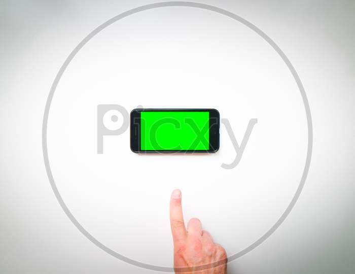 Woman Hand Holds Mobile Smartphone With Green Screen In Vertical Position Isolated On Green Background With Thumbs Up Finger. Mock Up Mobile Screen Blank Space
