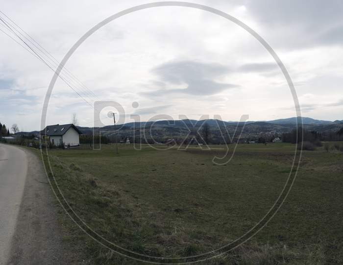 Panorama Shot Of A Country Road Bending Or Turning Showing Beautiful Landscape Along With A Wooden Farm House. Tymbark Village Located In Limanowa, South Poland.