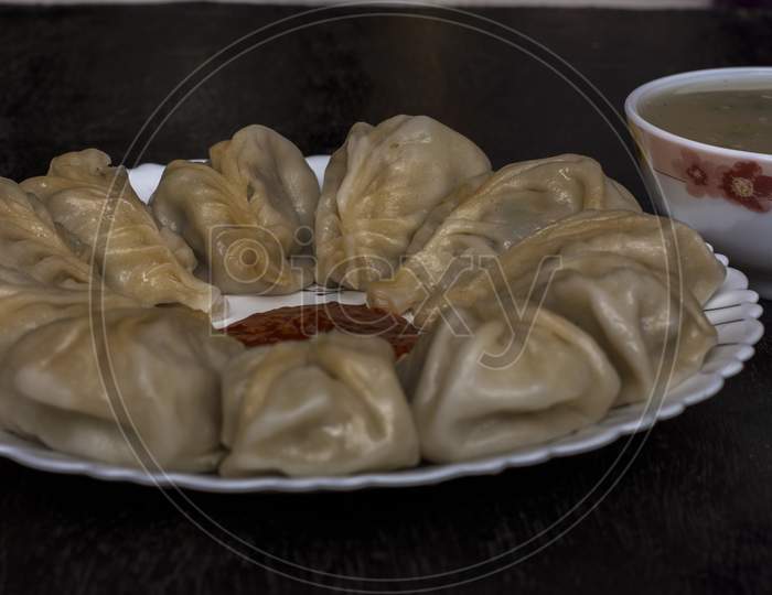 A Plate Full Of Chicken Momo With Sauce And Soup On A Black Background.