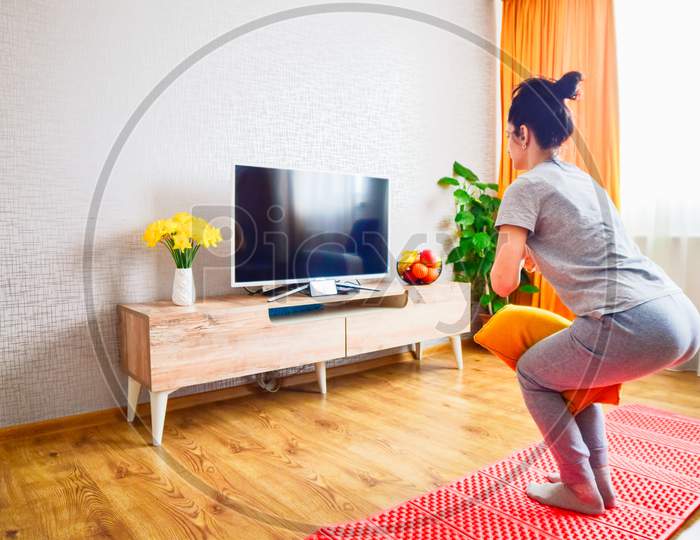 Young Beautiful Slim Athletic Caucasian Woman In Living Room On Mat Exercise Follow Tutorial On Smartphone With Yellow Pillow Tension Knees.