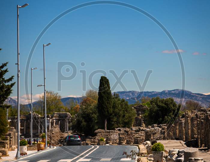 A Beautiful Tourist Street With An Empty Road Soaked With Old Stones And Planted Palm Trees Against The Backdrop Of The Old Ruined City In Sida, Turkey