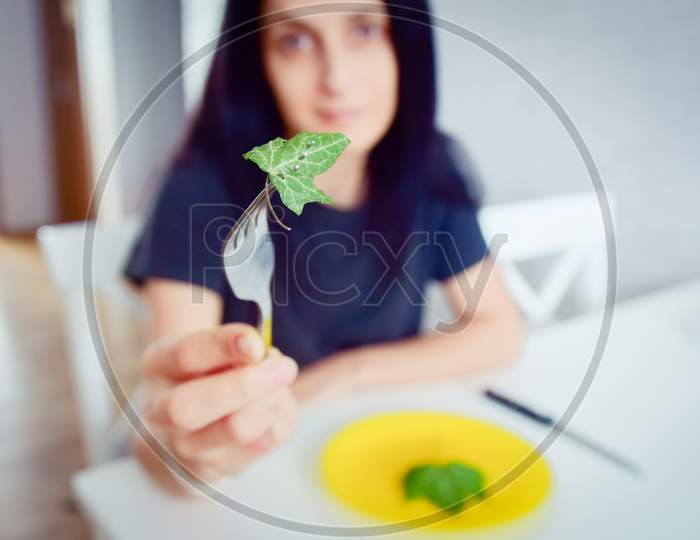 Close Up View Slim Female Hold Fork With Leaf In Kitchen On Diet. Extreme Starvation For Slim Body And Diet Concept.