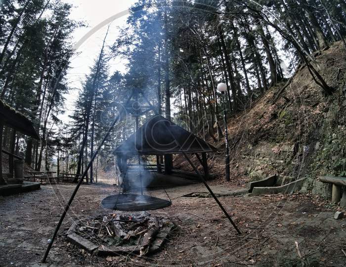South Poland: Barbecue Location In The Middle Of The Forest Surrounded With Tall Trees. Wilderness Wide Angle View Of Smoke Coming From Fire Against Abandoned Shed In The Peaceful Environment