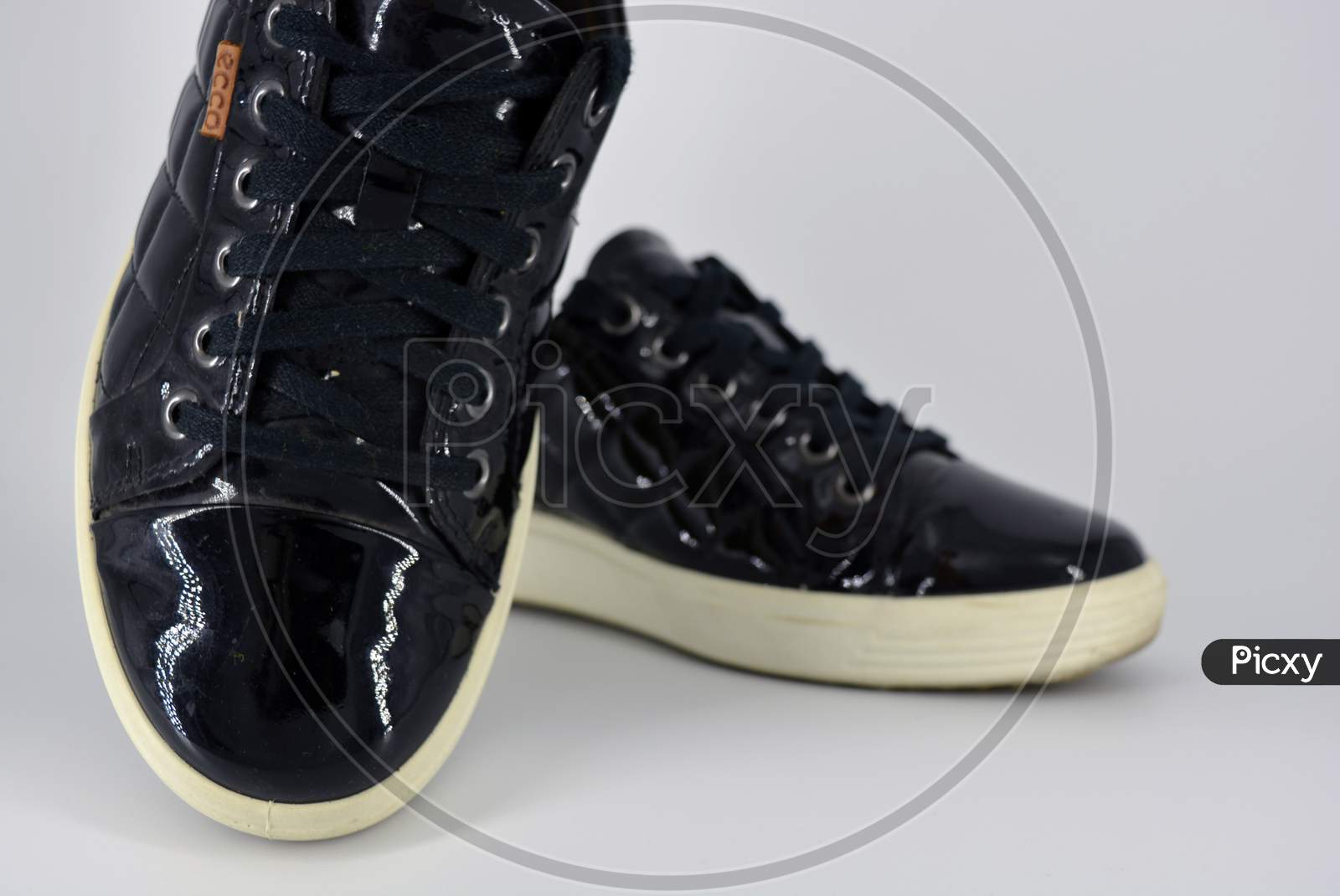 Stylish bright black lacquer shoes located on a white background. Moccasins made of genuine leather with bullshit and black wide laces. Women's sneakers on a white tast sole.