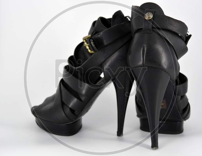 Black sandals on a thin high heel arranged on a white background. Stylish women's shoes made of genuine leather. Evening sandals with beautiful golden insole and twisted leather ribbon.
