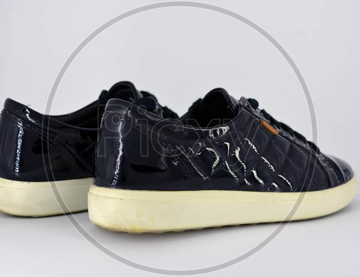 Stylish bright black lacquer shoes located on a white background. Moccasins made of genuine leather with bullshit and black wide laces. Women's sneakers on a white tast sole.