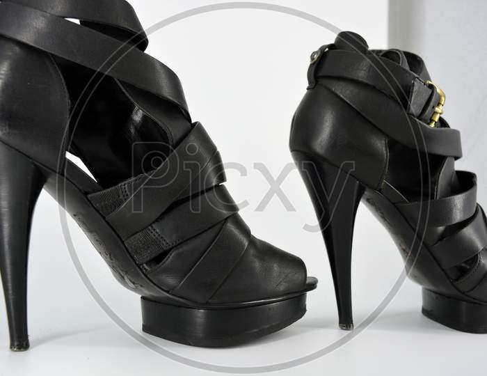 Black sandals on a thin high heel arranged on a white background. Stylish women's shoes made of genuine leather. Evening sandals with beautiful golden insole and twisted leather ribbon.