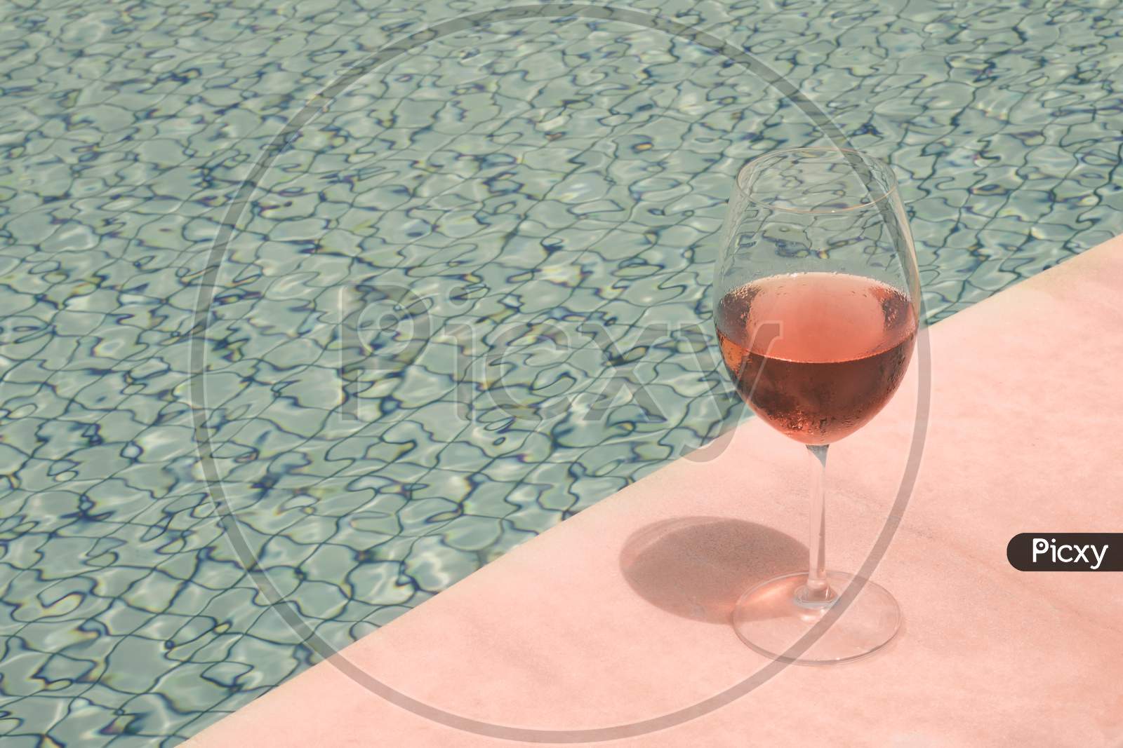Crystal Goblet With Rose Wine On The Edge Of A Swimming Pool. High Class People Drink Concept.