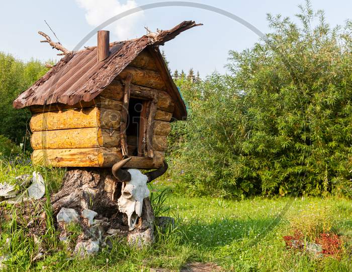 Close-Up Of A Toy Wooden House On Chicken Legs With A Skull Of An Animal Buffalo Decorations For The Garden On A Garden Stone On A Green Grass Background On A Warm Summer Day.The House Of Baba Yagi From Fairy Tales
