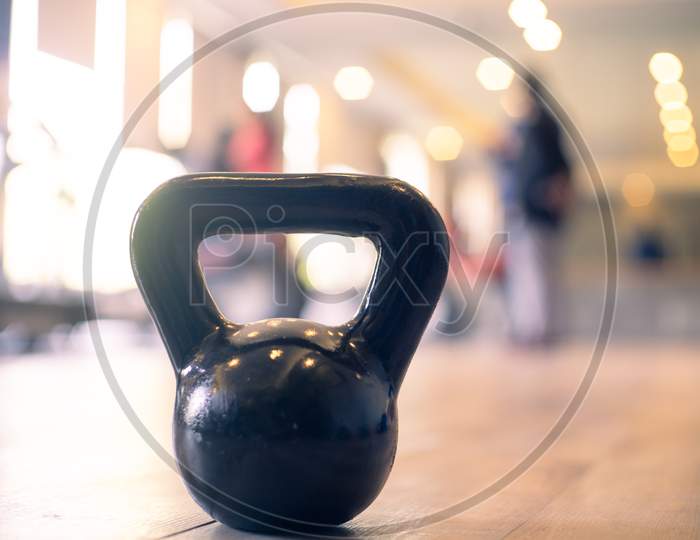 Panning Shot Showing A Kettleball In Focus With Out Of Focus People In A Gym With Bright Lights Excercising As Part Of A Healthy Lifestyle And Immunity And Recovery From The Coronavirus Pandemic