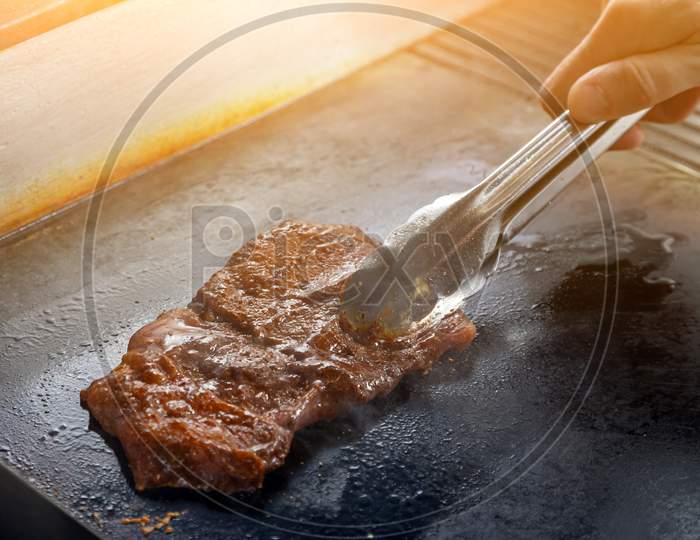 Close-Up Male Chef Cook Fries On A Large Professional Stove A Large Pickled Piece Of Meat. The Process Of Frying Meat