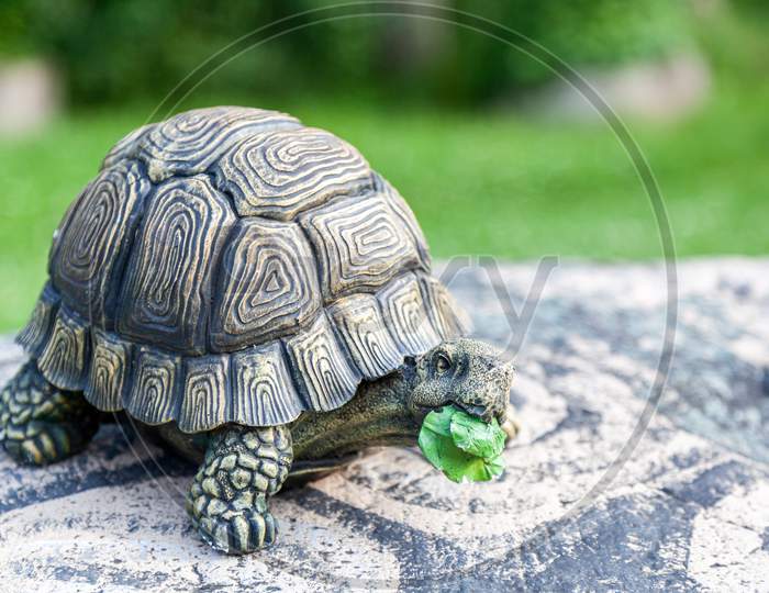 Close-Up Of A Large Turtle In A Stone Shell - Decorations For The Garden On A Garden Stone On A Green Grass Background On A Warm Summer Day