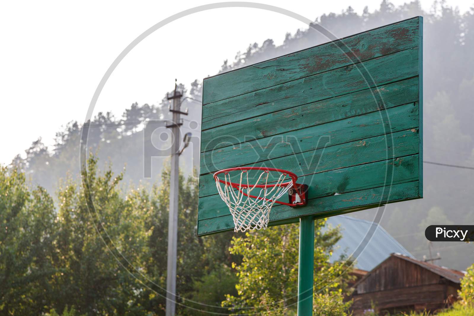 Basketball Green Old Ring With A Net For Playing Basketball Outdoors, In The Background A Green Forest On A Warm Summer Day