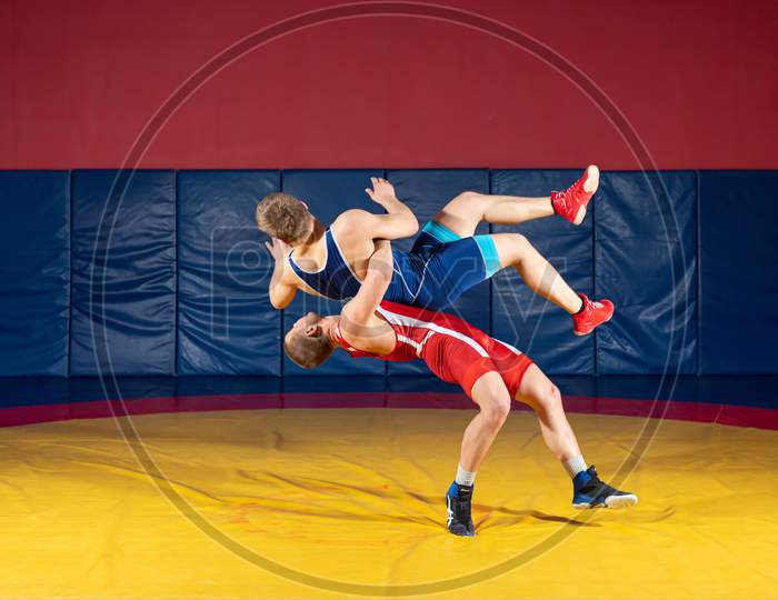 The Concept Of Fair Wrestling. Two Greco-Roman  Wrestlers In Sportwears Makes Throw Through The Back On A Wrestling Carpet In The Gym.The Concept Of Male Wrestling And Resistance
