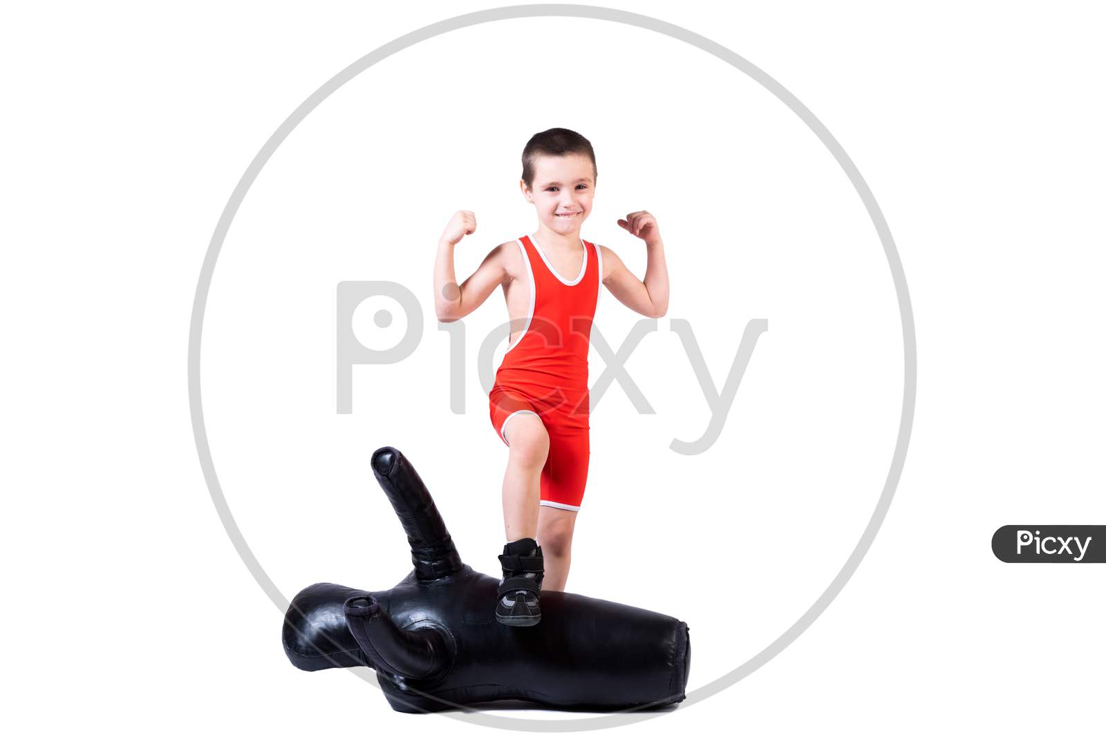 Cheerful Sports Boy In Wrestling Tights And Wrestling Shows Biceps, Rejoices In Victory, Stands Over A Defeated Sports Dummy For Training And Handling Techniques From Various Martial Arts On A Fir-Tree Isolated Background.