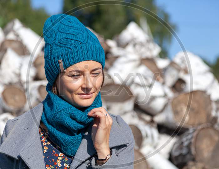 Portrait Of A Beautiful Young Model In Knitted Hat  And Warm Clothes Enjoy Day, On Background Birch Logs . Autumn Warm Photo. Woman Smiling And Look Away, Joyful Cheerful Mood.