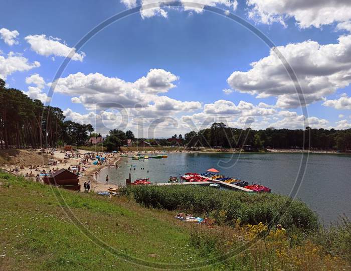 Wide Angle Shot Of A Man Made Lake Lagoon Named Kryspinow With Water Ride Boats And People Located In A Village In The District Of Gmina Liszki, Lesser Poland Voivodeship Against Clouds During Summer