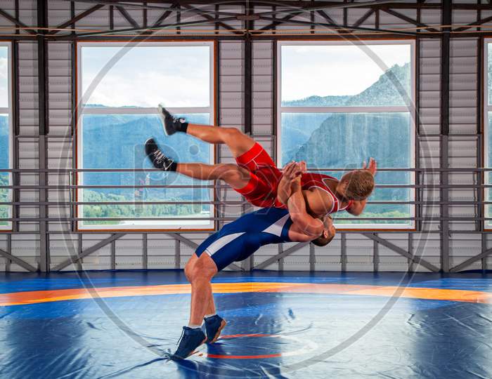 Greco-Roman Wrestling Training, Grappling. Two Greco-Roman  Wrestlers In Red And Blue Uniform Wrestling  On A Wrestling Carpet In The Gym.Training And Practicing Sports Throws