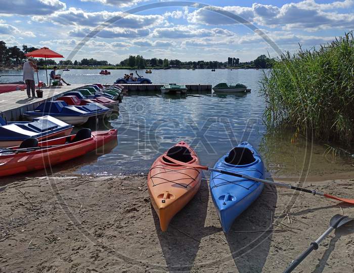 Krakow, Poland - May 05, 2021: Wide Angle Shot Of Couple Of Kayak For Rent Kept At Dock With It'S Paddle In The Man Made Lake Lagoon Named Kryspinow Against Dramatic Clouds