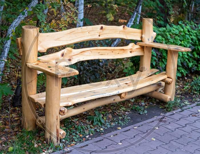 Beautiful New Wooden Bench Made Of Cedar Stands In The Park On A Background Of Green Trees