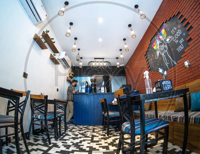 Fisheye Wideangle Shot Of Man Standing At A Posh Upmarket Cafe Restaurant Opening For Business Empty Chairs And Tables With Person Wearing A Mask