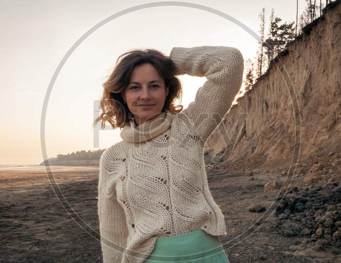Posing Woman In Nature. Young Woman In Stylish Clothes: Knitted Sweater And Long Skirt Posing Against The Backdrop Of A Sand Pit, The Sea. Photos On Vacation In The Fall