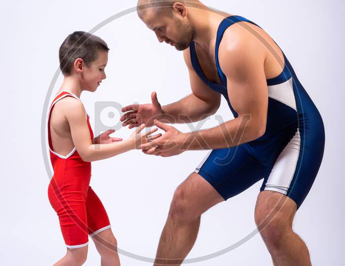A  Wrestler Boy In A Sports Tights Wrestles With An Adult Male Wrestler On A White Isolated Background. The Concept Of Child Power And Martial Arts Training. Teaching Children Greco-Roman Wrestling
