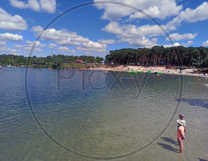 Krakow, Poland - May 05, 2021: Couple Of People Standing On A Kryspinow Man Made Lake Lagoon Water In The District Of Gmina Liszki, In Lesser Poland Voivodeship Against Dramatic Clouds During Summer
