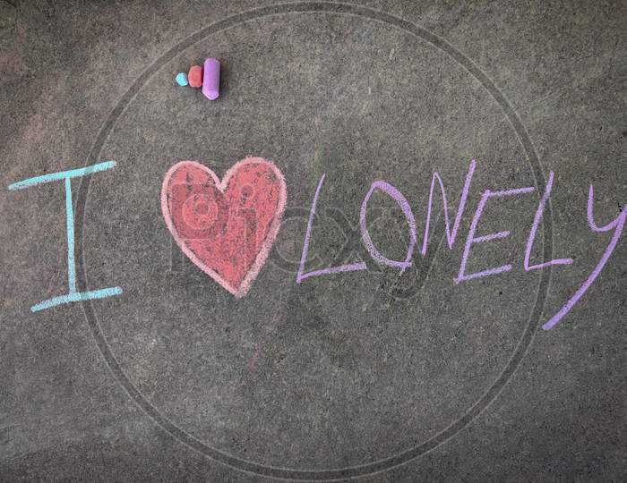 The Inscription Text On The Grey Board, I With Hand Drawn Love Symbol And Lonely . (I Love Lonely). Using Color Chalk Pieces.