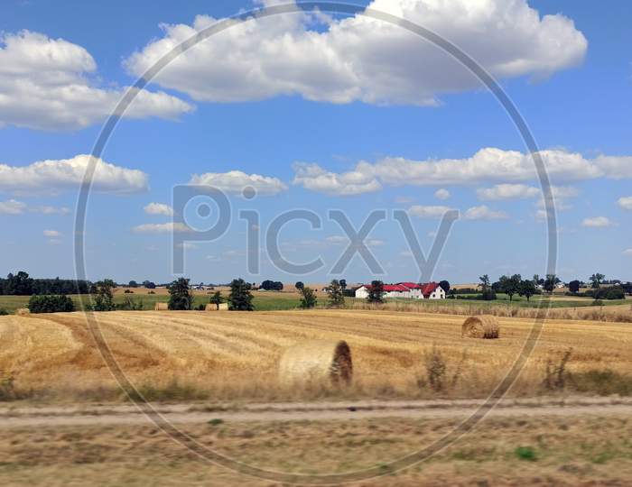 Panorama Of Country Side Across Green Grass Field Of Cut And Rolled Hay Near North Poland Against Dramatic Clouds And Blue Sky. Country Side Background.