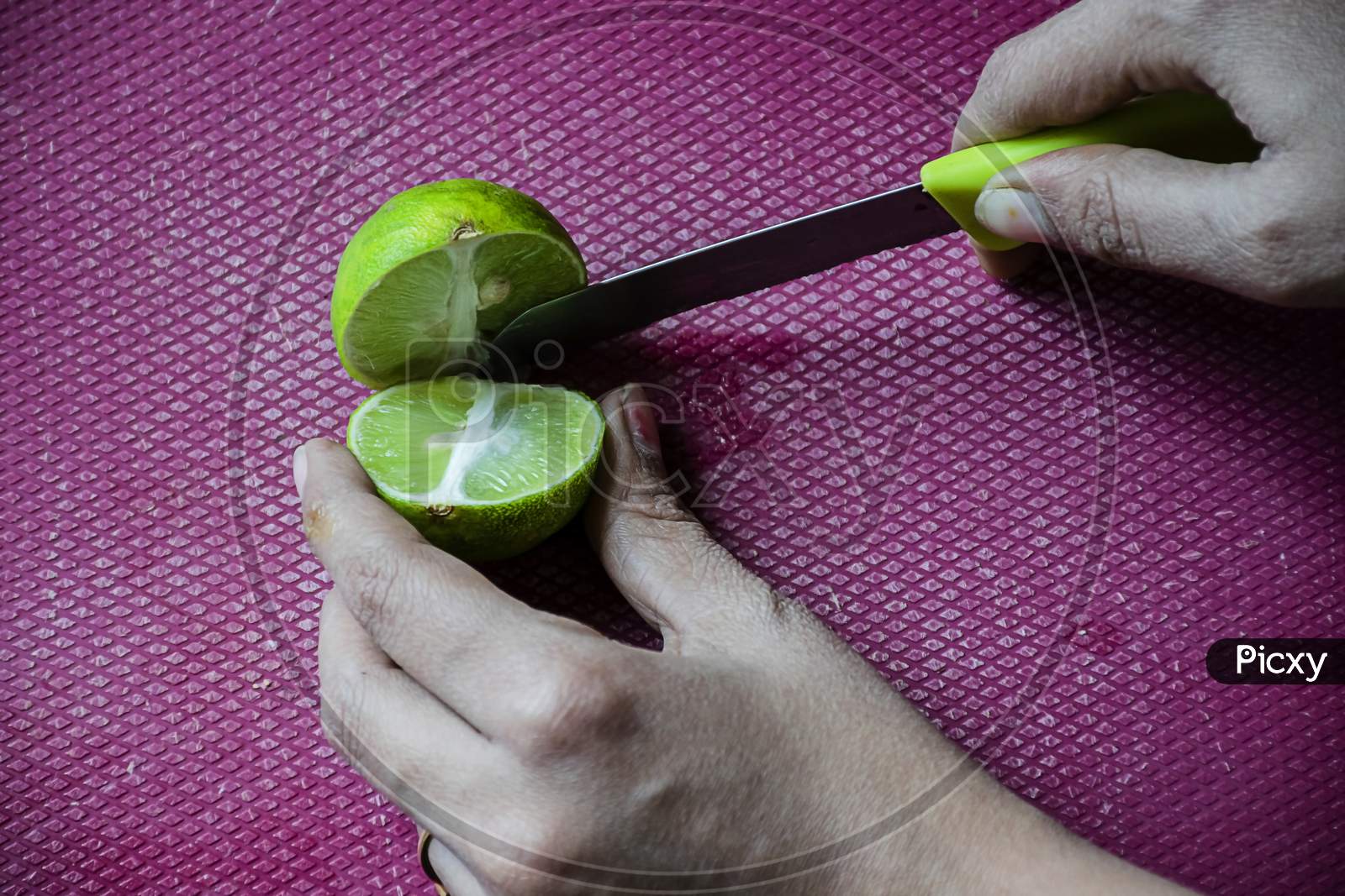 Stock Photo Of Women Cutting Fresh Juicy Lemon On Purple Color Chopping Board With Yellow Color Knife , Focus On Object. Blur Background.