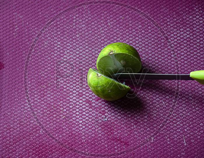Stock photo of women cutting fresh juicy lemon on purple color chopping board with yellow color knife , focus on object. blur background.