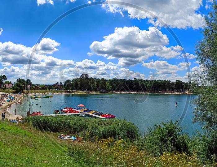 Wide Angle Panorama Shot Of A Man Made Lake Lagoon Named Kryspinow With Water Ride Boat And People Tanning, Located In A Village In District Of Gmina Liszki, Lesser Poland Voivodeship