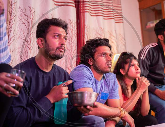Group Of Young Millennial Friends Interestingly Watching Sports Or Movie While Sitting On Sofa At Home - Concept Of Sports Fans, Nail Biting Game Or Web Series.