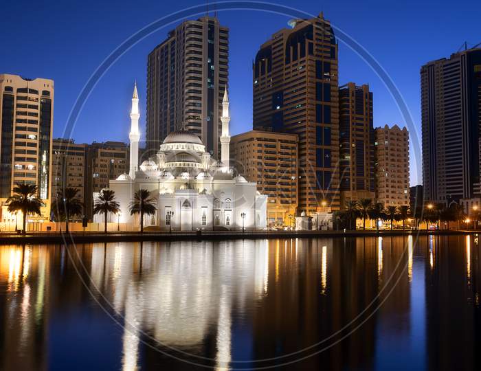 View Of The Beautifully Illuminated Al Noor Mosque During The Early Sunrise Hours Showing Reflections In Water Captured From The Al Noor Island Sharjah, Uae.