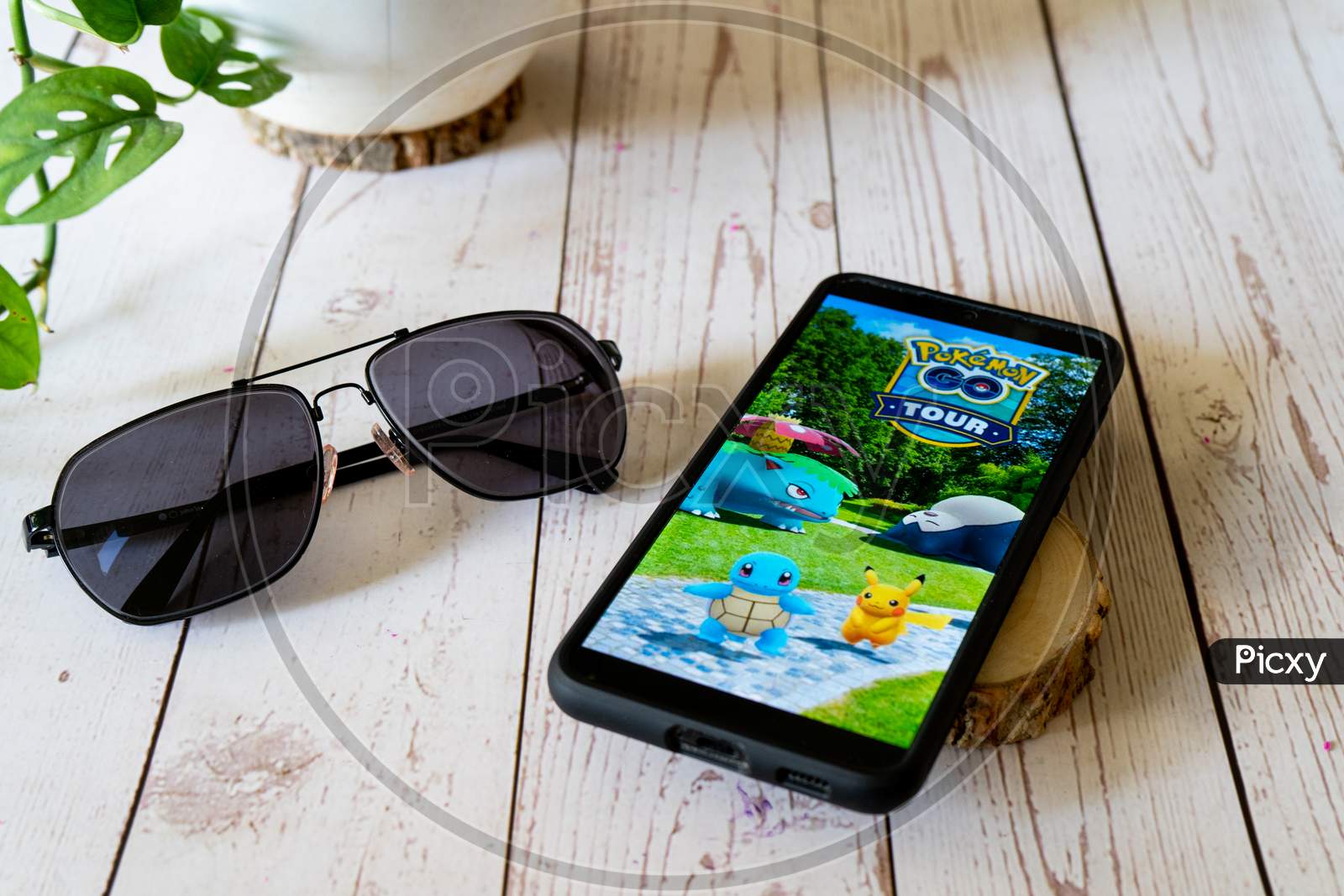 Famous Augmented Reality Virtual Game Pokemon Go Tour Playing On A Mobile Phone On A Wooden Table Outdoors With Plants Goggles Showing People Enjoying This Multiplayer Game