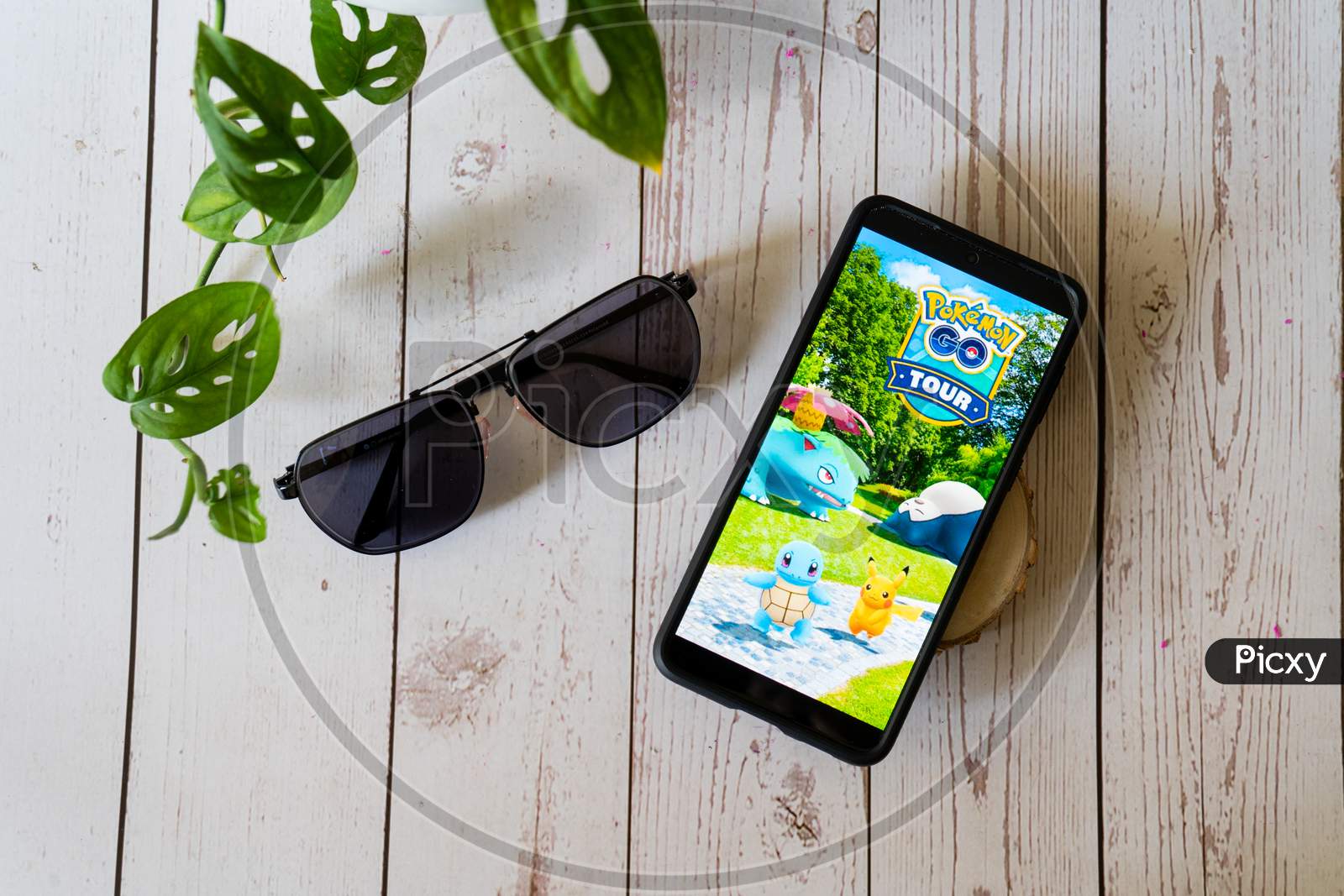Famous Augmented Reality Virtual Game Pokemon Go Tour Playing On A Mobile Phone On A Wooden Table Outdoors With Plants Goggles Showing People Enjoying This Multiplayer Game