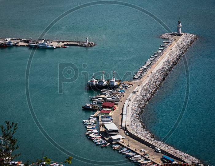 Top View Of A Pier  With A Beautiful White Lighthouse And A Pier With Many Boats And Yachts On The Background Of The Blue Sea