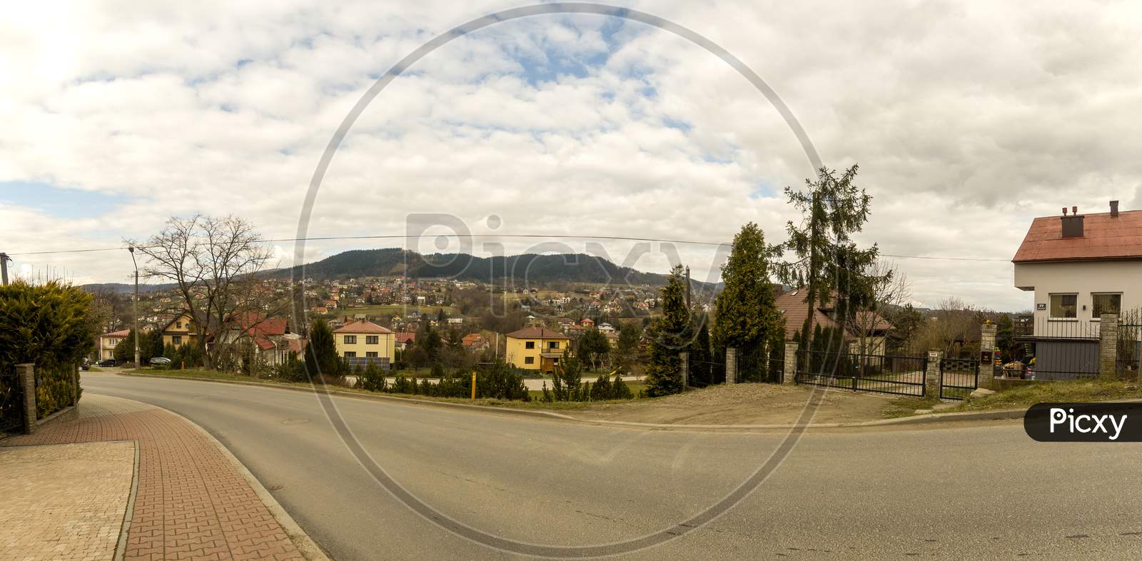 Limanowa, South Poland - April 01, 2021: Panorama View Of Houses Showing Countryside Life In Polish Village Against Polish Mountains And Dramatic Clouds.