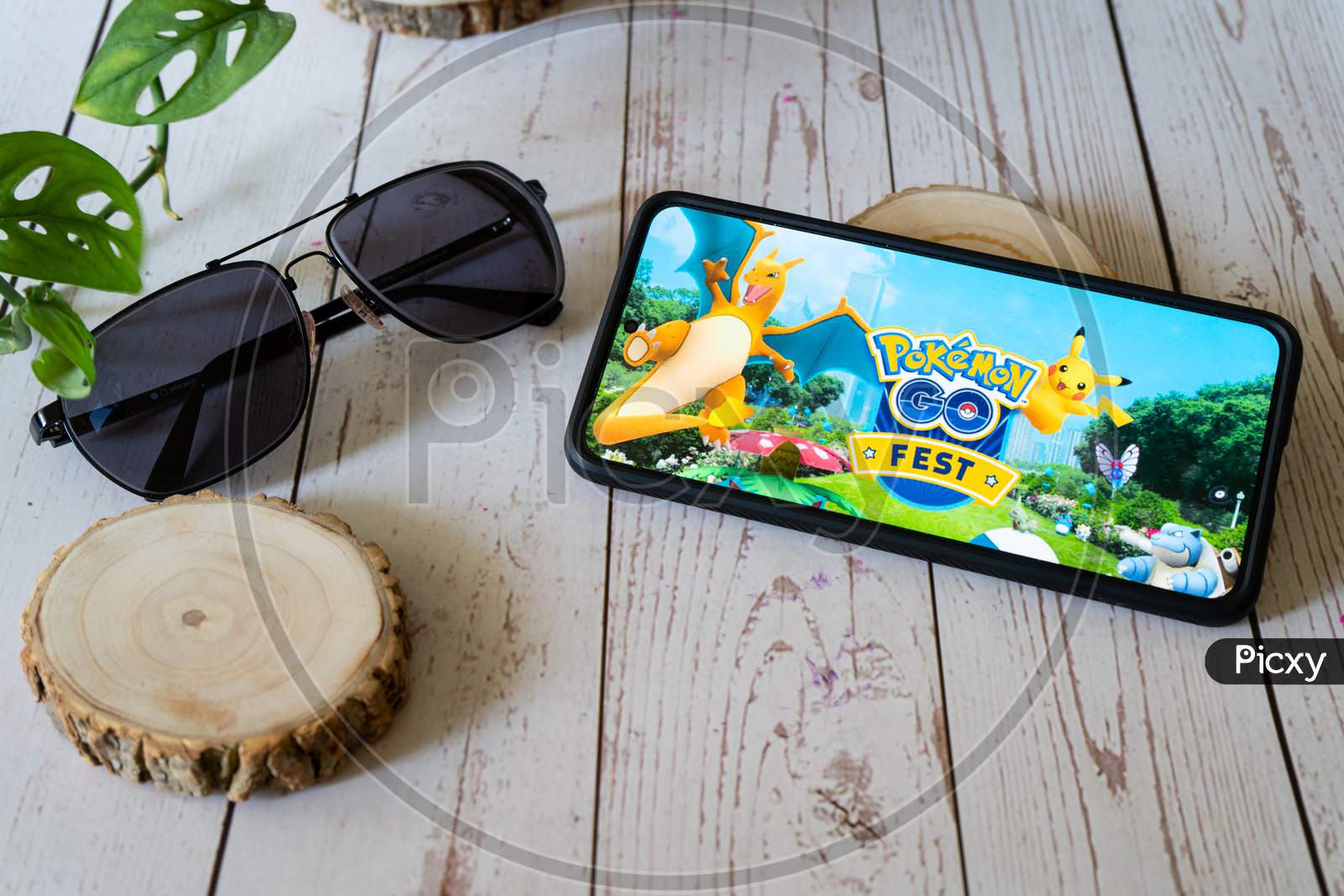 Famous Augmented Reality Virtual Game Pokemon Go Fest Playing On A Mobile Phone On A Wooden Table Outdoors With Plants Goggles Showing People Enjoying This Multiplayer Game
