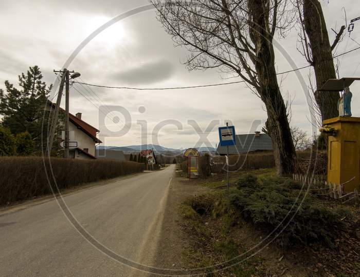 Limanowa, South Poland - April 01, 2021: View Of Country Side Showing Narrow Road And Bus Stop Located In Lysa Gora Beskid Wyspowy In The Polish Mountains